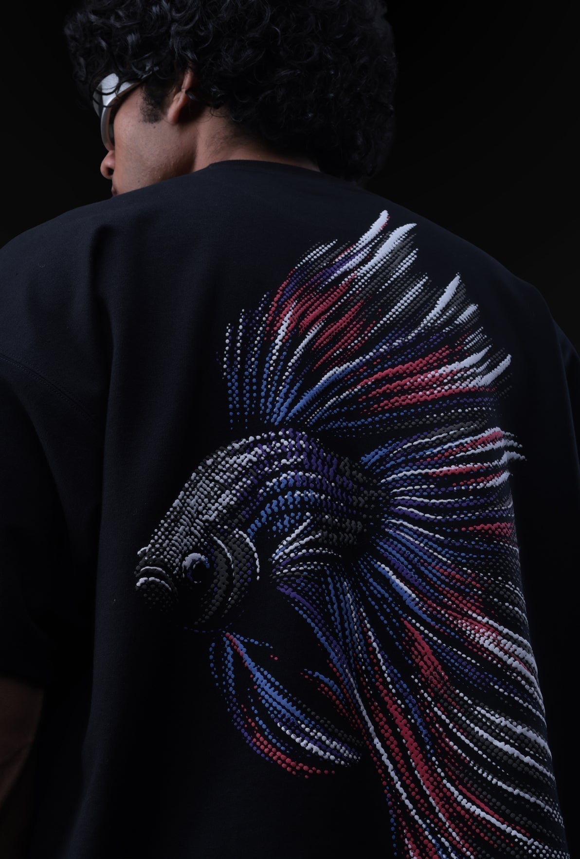 Person wearing a black shirt with a colorful fish design on the back against a dark background Crepdog Crew