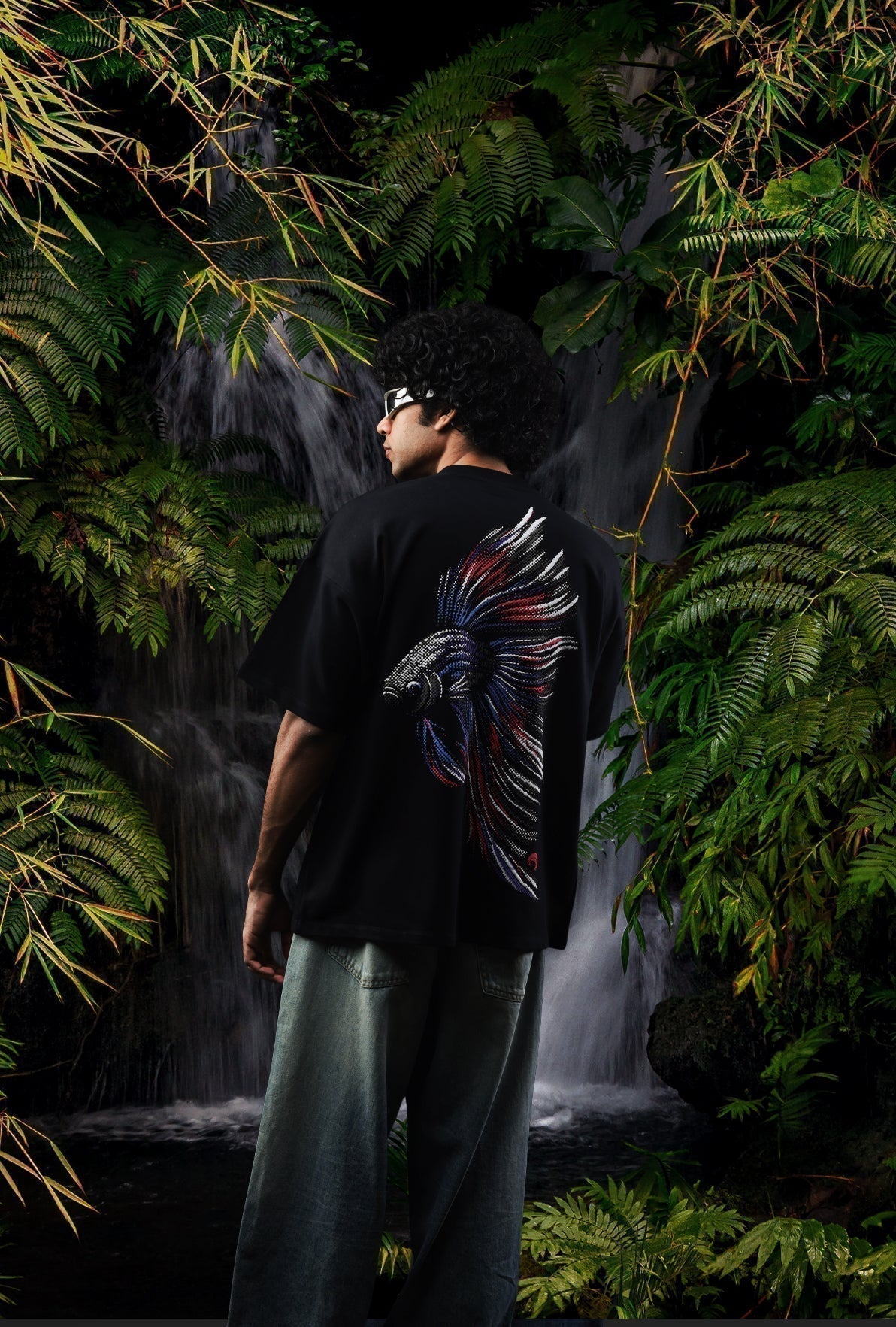 Person wearing a black t-shirt with a colorful fish design in a lush, dark forest setting Crepdog Crew