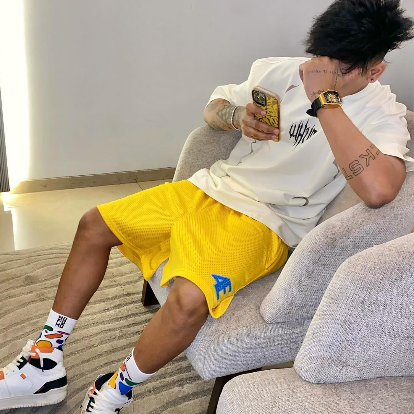Person sitting on a couch wearing a white shirt, yellow shorts, and colorful socks - Crepdog Crew