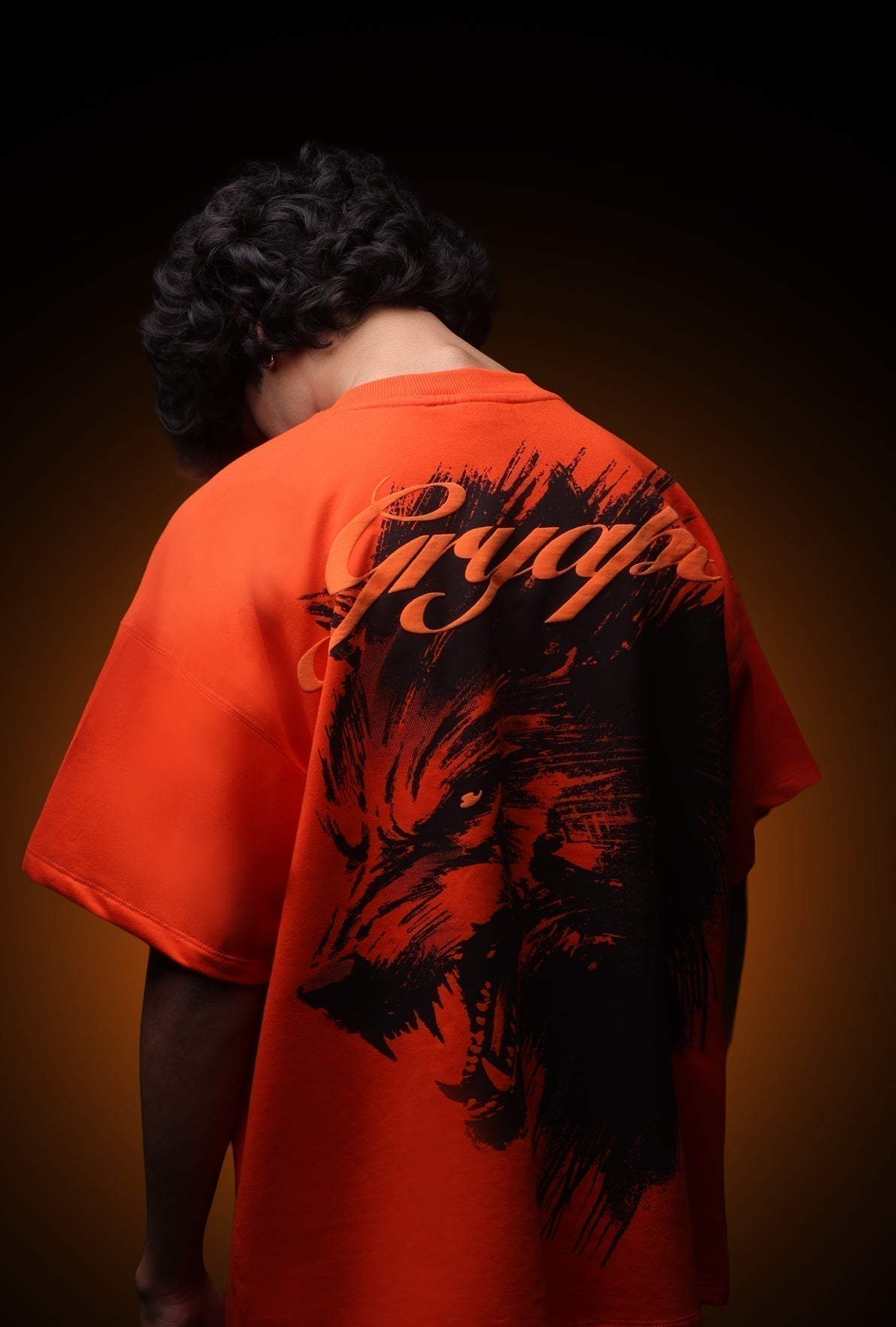 Person wearing an orange t-shirt with a black graphic design on the back against a dark background - Crepdog Crew