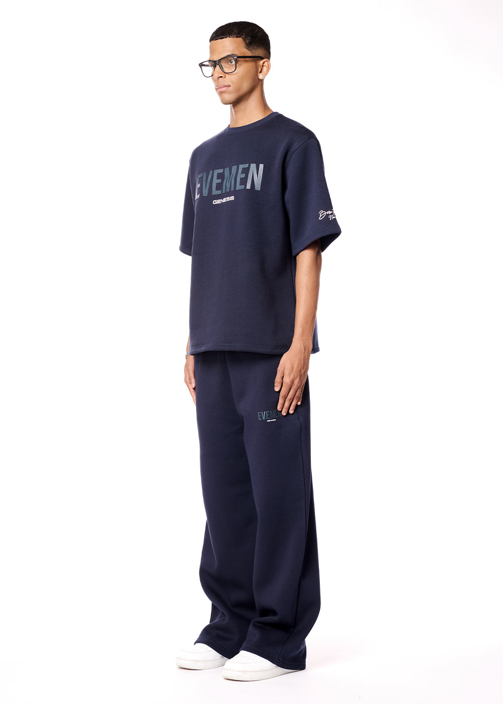 Man wearing a navy blue oversized t-shirt and pants with 'EYEMEN' branding on a white background