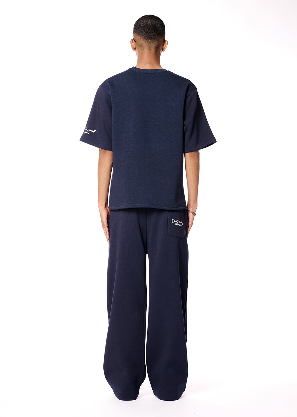 Person wearing navy blue t-shirt and pants with brand logo on a white background