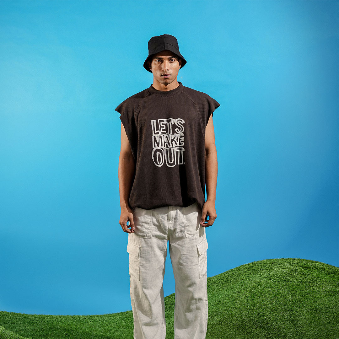Person wearing a sleeveless brown shirt with text, standing against a blue sky with green grass at the bottom Crepdog Crew