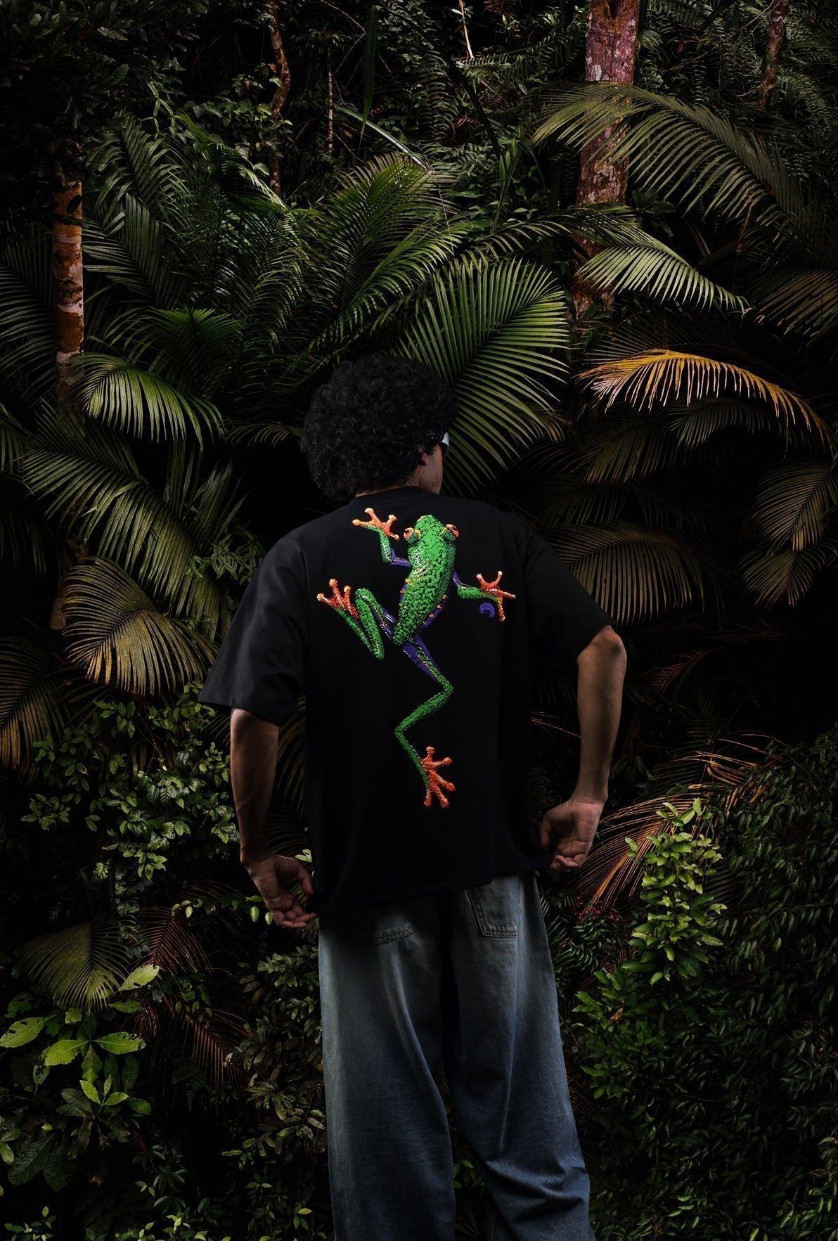 Person wearing a black t-shirt with a colorful frog design, standing in a dense forest Crepdog Crew