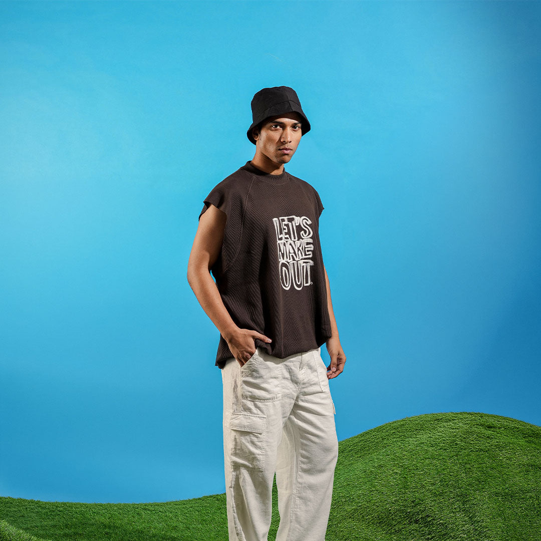 Person wearing a sleeveless shirt with text and white pants standing on grass with a blue sky background Crepdog Crew